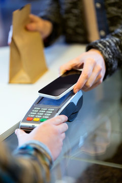 Customer using her smartphone to make mobile payment with electronic reader.
