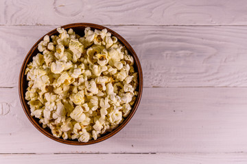 Ceramic bowl with popcorn on wooden table. Top view