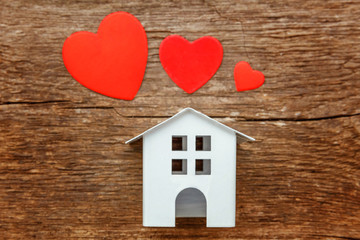 Miniature white toy house with red hearts on a rustic old vintage wooden background. Mortgage property insurance dream home concept
