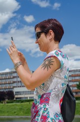 A woman in a gown and sunglasses is taking a picture of her cell phone.