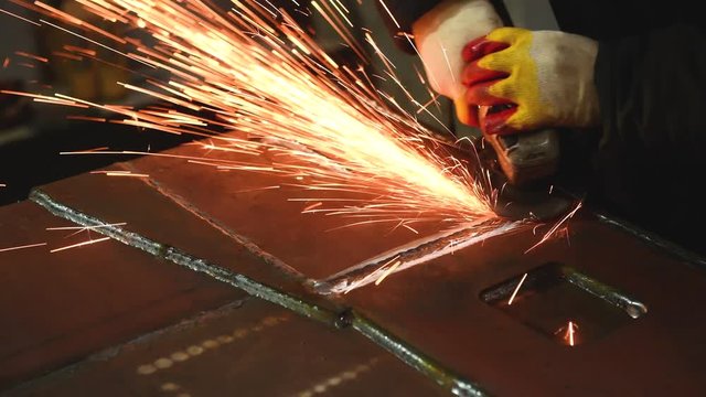worker grinding weld seam with grinder machine and sparks