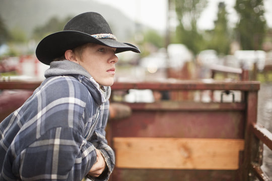 Teen wearing cowboy hat, looking over fence into rodeo arena.