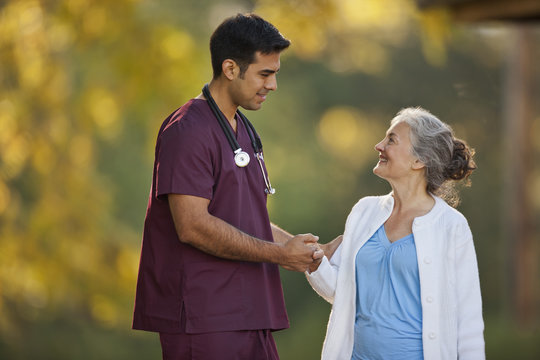 Smiling senior woman and a male doctor having a conversation while holding hands in a park.