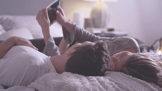 Young loving couple kiss while laying on their bed 