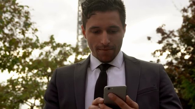 Attractive young man in a suit using application on a smartphone next to the Eiffel Tower
