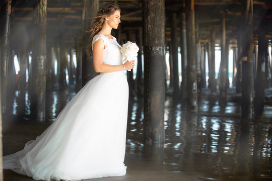 Beautiful portrait of bride standing alone in flying white dress outdoors near ocean
