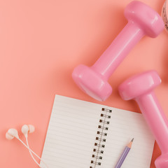 Styled stock photography of fitness equipment dumbbells notepad pencil and earphone on pink background. Flat lay.
