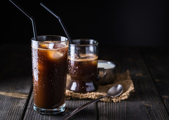 Ice coffee in a tall glass on dark natural desk.