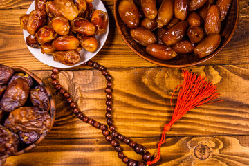 Date fruits and rosary on wooden table. Top view