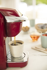 Red coffee maker drinks coffee into a small ceramic cup