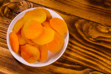 Ceramic plate with dried apricots on wooden table. Top view
