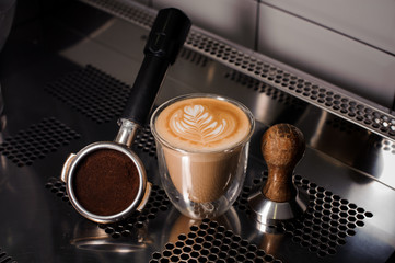 Tamper and coffee cup filled with decorated latte on the counter