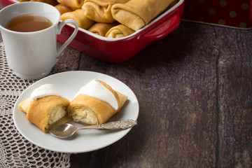 Pancakes stuffed with cottage cheese with sour cream and cup of tea. Breakfast. Sweet dessert of pancakes rolls.