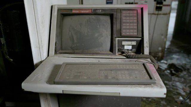 A pan shot of an old, dusty computer in an abandoned factory.
