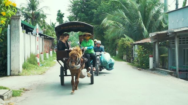 A motorcycle holding huge bags rides next to a group of tourists in a horse drawn carriage