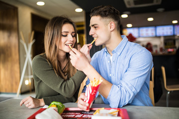 Happy caucasian couple eating french fries in fast food and have fun