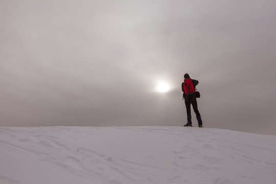 Man taking photo of pale sun on a snowy slope in a gray day, Col Visentin, Belluno, Italy