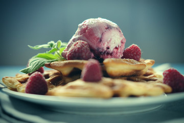 Waffles with raspberry ice cream and fresh raspberries, decorated with mint over blue wooden background