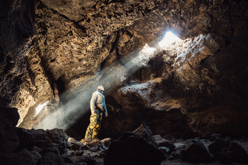 Man standing under the light in the mountain cave. Extreme adventure travel concept.