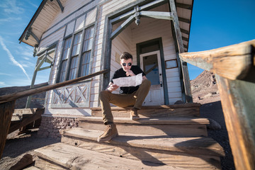 Stylish farmer man reading the map sitting on the porch of his house at hot summer day