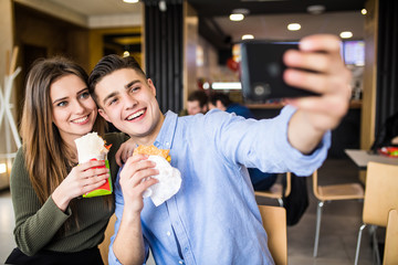Happy smiling woman and a handsome man are enjoying their delicious and tasty burgers and doner taking selfie phone