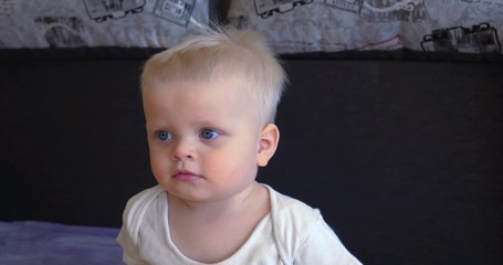 Toddler boy sitting on the couch, blond, blue eyes, watching TV.