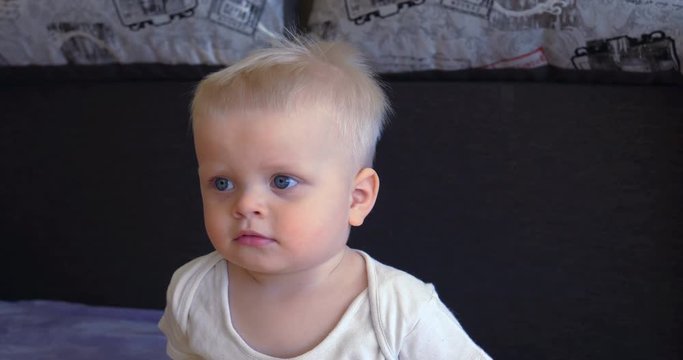 Toddler boy sitting on the couch, blond, blue eyes, watching TV.