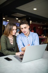 Happy young couple is using a laptop, drinking coffee and smiling while sitting at the cafe