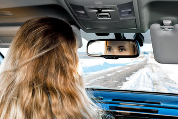 in the car on the winter road you can see the eyes in the rear-view mirror of the blonde girl sitting behind the wheel