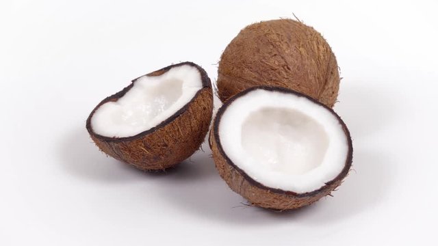 One whole ripe brown tropical coconut and two halves with yummy white pulp rotating on white isolated background. Healthy fresh tropical fruits. Loopable seamless cocos rotating