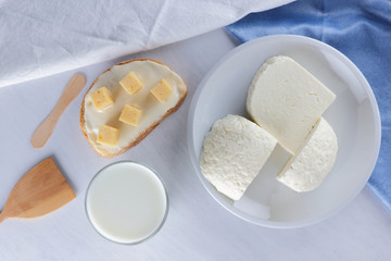 Cheese, dairy assortment on a white background, sandwich with soft cheese on a blue napkin, wooden background, wooden cutlery, top view, white cheese on a white plate, kefir in a glass, pop art