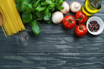 Pasta cooking ingredients. Raw spaghetti, tomatoes, basil, olive oil, mushrooms and spices  flat lay on rustic wooden table with free space. Italian cuisine food background concept