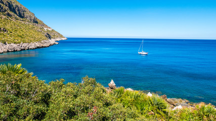 A sailing boat into the turquoise Mediterranean Sea, at San Vito Lo Capo, Sicily, Italy.