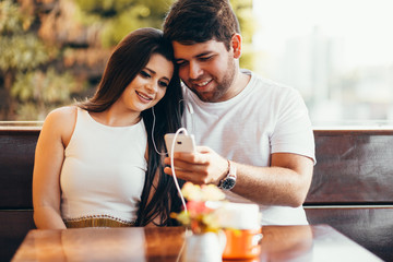 Portrait of couple using smartphone and listening to music in cafeteria or restaurant