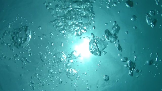 UNDERWATER: Countless air bubbles floating towards the surface of breathtaking turquoise sea. Cinematic shot of droplets swimming from the depths of tranquil ocean towards the bright tropical sun.