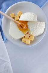 Cheese, milk assortment on white background, white cheese and honey on a blue napkin, wooden background, wooden stick for honey, top view, cheese on white plate, kefir in a glass, pop art