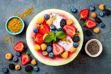 Healthy summer breakfast concept, fruit salad in carved watermelon. Watermelon bowl with yogurt, chia seeds, fresh berries, bee pollen.