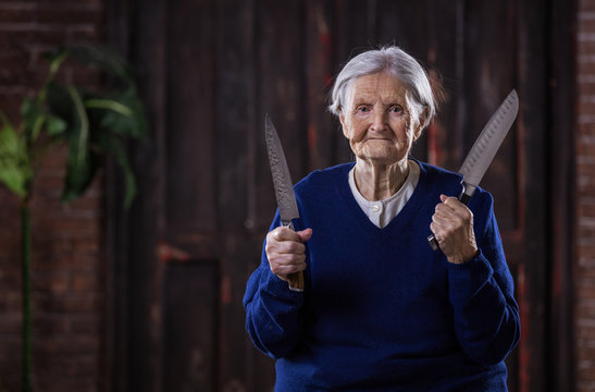 Senior woman holding kitchen knives indoors. Self defense concept.