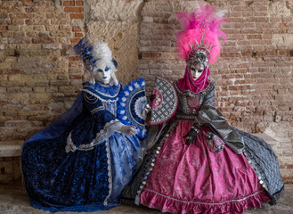 Fototapeta na wymiar Masked women in ornate blue and pink costumes with fans in an inner courtyard during the Venice Carnival (Carnivale di Venezia)