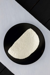 Cheese, soft cheese on a black plate, wooden table, black and white color, minimalism, Italian cuisine, copy space, dairy product on a wooden board, art