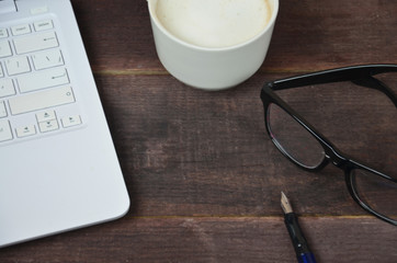 laptop and glasses, pen and notebook on wooden table, coffee Cup in the background