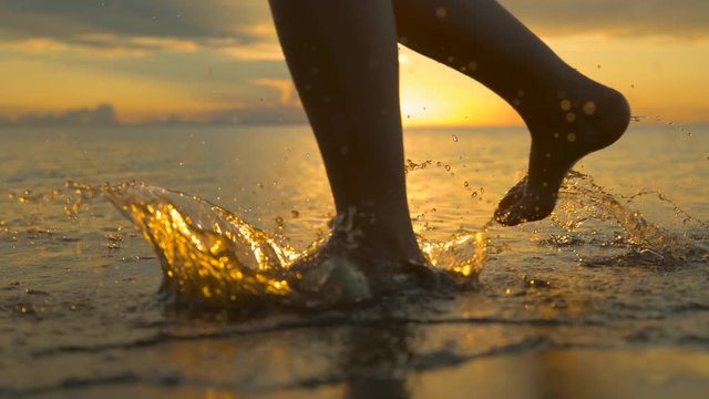 SLOW MOTION, CLOSE UP: Unrecognizable woman jogs barefoot along sunlit tropical beach. Young female on relaxing vacation exercises at the seaside on idyllic golden morning. Picturesque tropical sunset