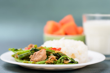 Thai food, stir fried morning glory (Pad Pak Boong) with cooked rice on dish, glass of milk and piece of ripe papaya