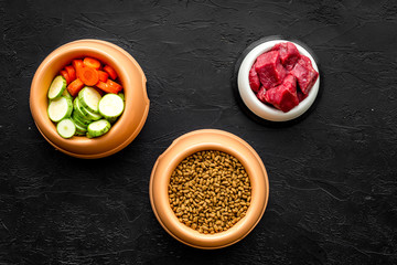 Dry pet food with natural ingredients. Raw meat, cut vegetables zucchini and carrot on black backgroud top view mockup