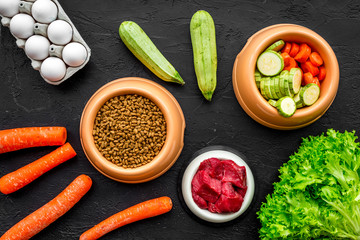 Dry pet food with natural ingredients. Raw meat, vegetables zucchini and carrot near eggs on black backgroud top view pattern