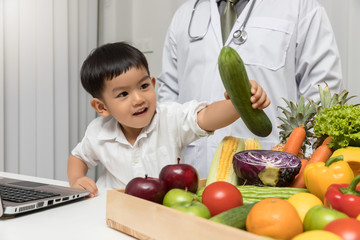 Healthy and nutrition concept. Kid learning about nutrition with doctor to choose eating fresh fruits and vegetables. Young asian boy holding cucumber.