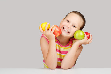 Cheerful little girl with apples and lemon poses positively in studio