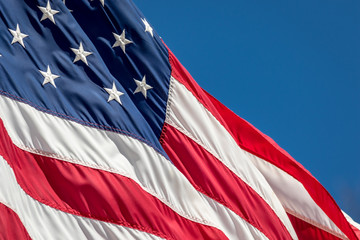 American Flag adorned with stars and stripes waves in the wind against a blue sky