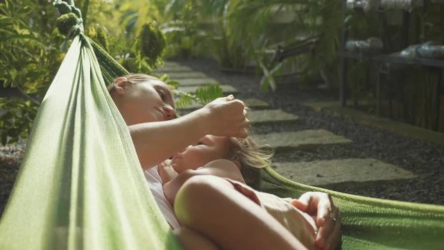 Young mother and daughter relaxing together in a hammock at garden in summer day