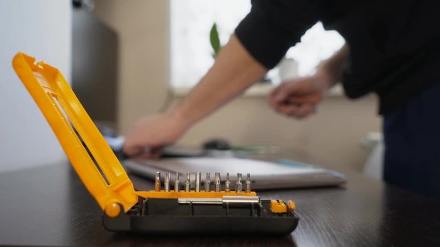 The wizard uses a screwdriver to twist the screw on the lid of the notebook.